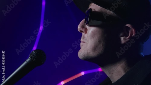 Close up of rap artist singing into a microphone for a music video on a dark background