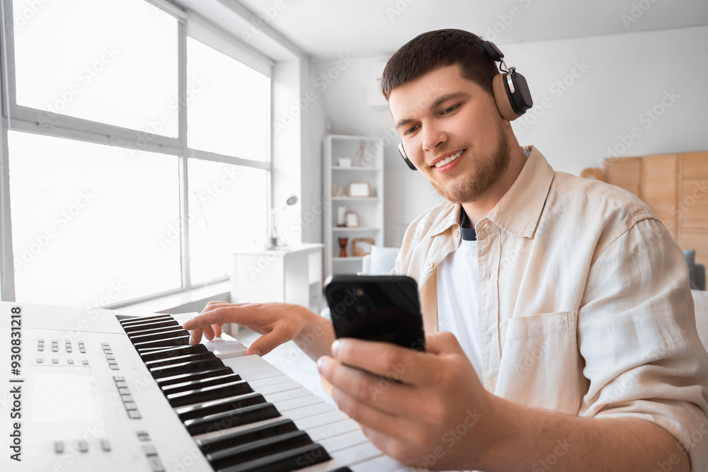 Young bearded man in headphones with mobile phone playing synthesizer at home Young bearded man in headphones with mobile phone playing synthesizer at home