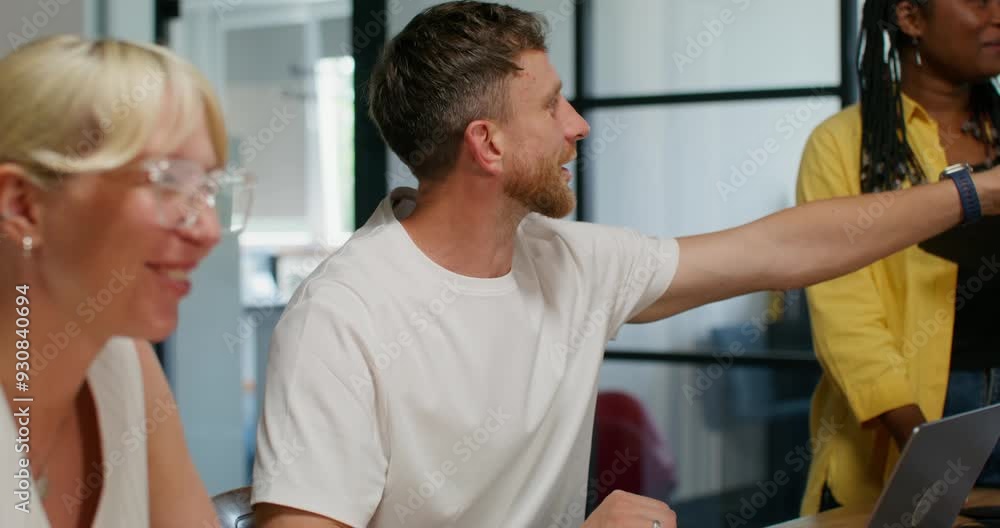 A man is talking sitting at a table at an office meeting next to his colleagues. The speaker stands in front of them A man is talking sitting at a table at an office meeting next to his colleagues. The speaker stands in front of them
