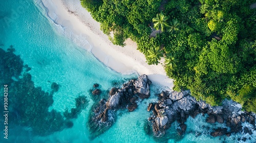 Aerial view of a tropical beach with clear turquoise water and lush green vegetation surrounding rocky formations.