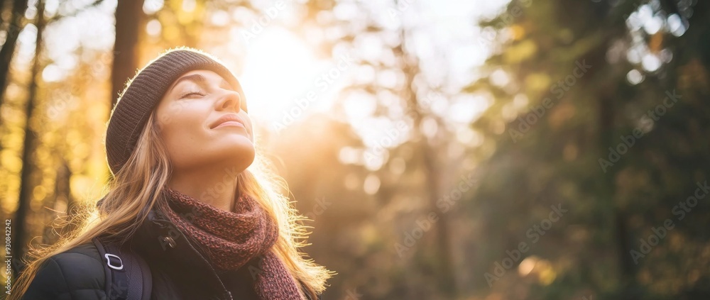 Woman in winter clothing stands in the forest with her eyes closed, breathing deeply and enjoying sunlight filtering through trees. Peaceful and happy expression with a warm golden glow. Woman in winter clothing stands in the forest with her eyes closed, breathing deeply and enjoying sunlight filtering through trees. Peaceful and happy expression with a warm golden glow.