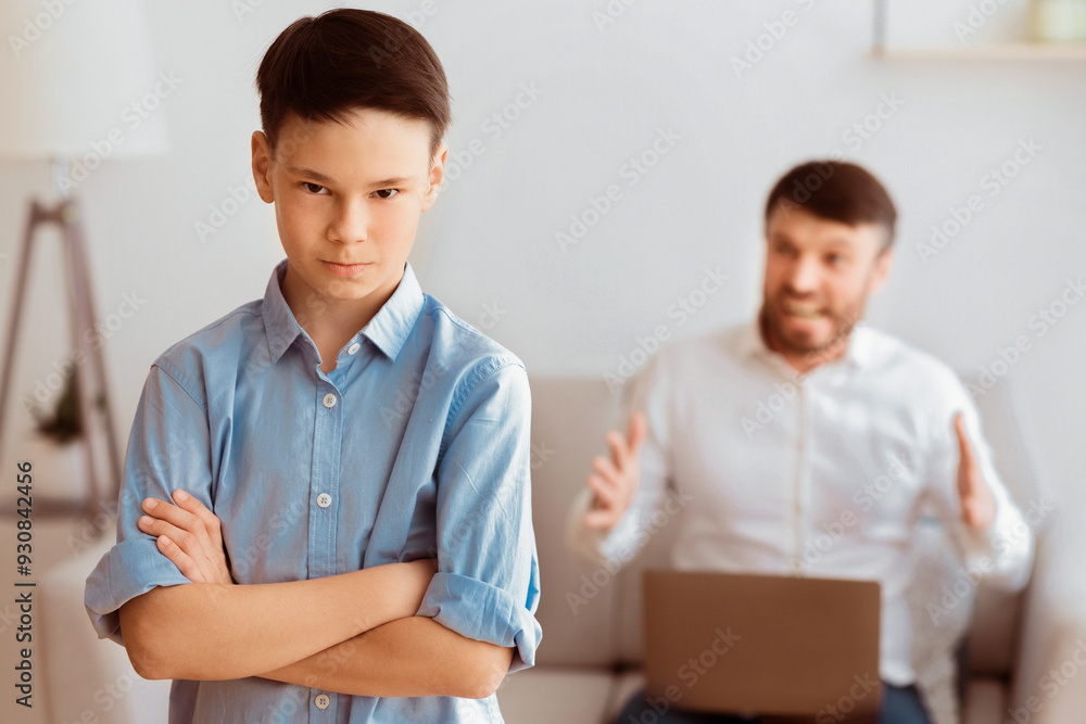 Furious Father Shouting At Son Sitting With Laptop On Sofa At Home. Family Problems Concept. Selective Focus Furious Father Shouting At Son Sitting With Laptop On Sofa At Home. Family Problems Concept. Selective Focus