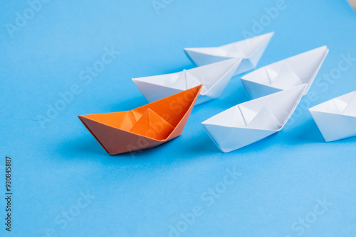 orange paper boat leading white boats on blue backgroun, leadership and business concept.
