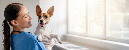 Bild auf Leinwand Smiling veterinarian in blue scrubs holds a joyful Jack Russell Terrier, ensurin