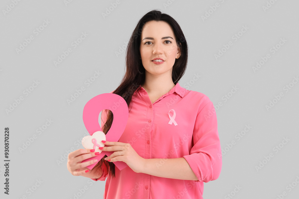 Young woman with pink ribbons and cookie on light background. Breast cancer awareness concept Young woman with pink ribbons and cookie on light background. Breast cancer awareness concept