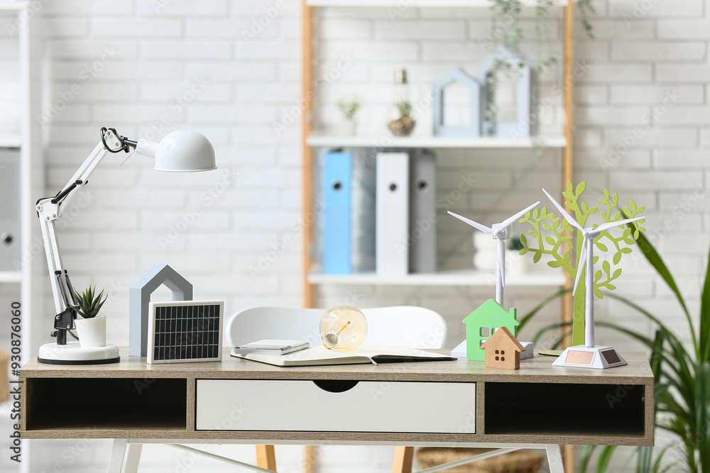 Wind turbine models with light bulb, house figures and solar panel on table in office. Green Energy concept Wind turbine models with light bulb, house figures and solar panel on table in office. Green Energy concept