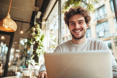 High-resolution brightly lit photorealistic candid photograph of a young marketer smiling while working on his laptop in a stylish office with natural light. The photograph is styled like a high-end photo