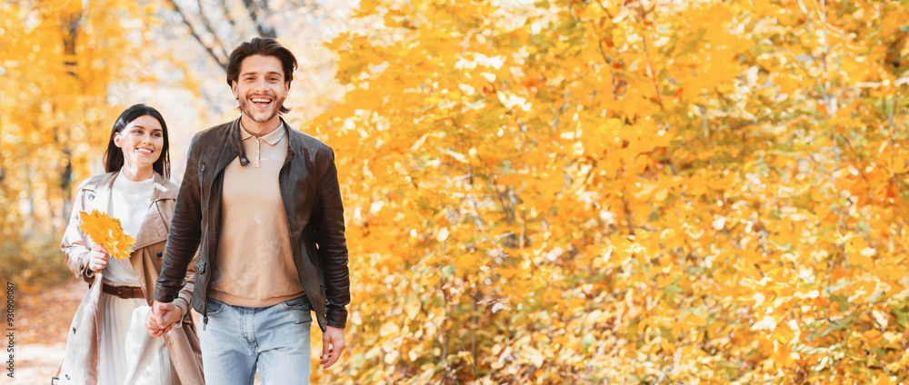 Obraz premium Excited guy showing his pretty girlfriend beautiful autumn forest, pulling her hand, copy space
