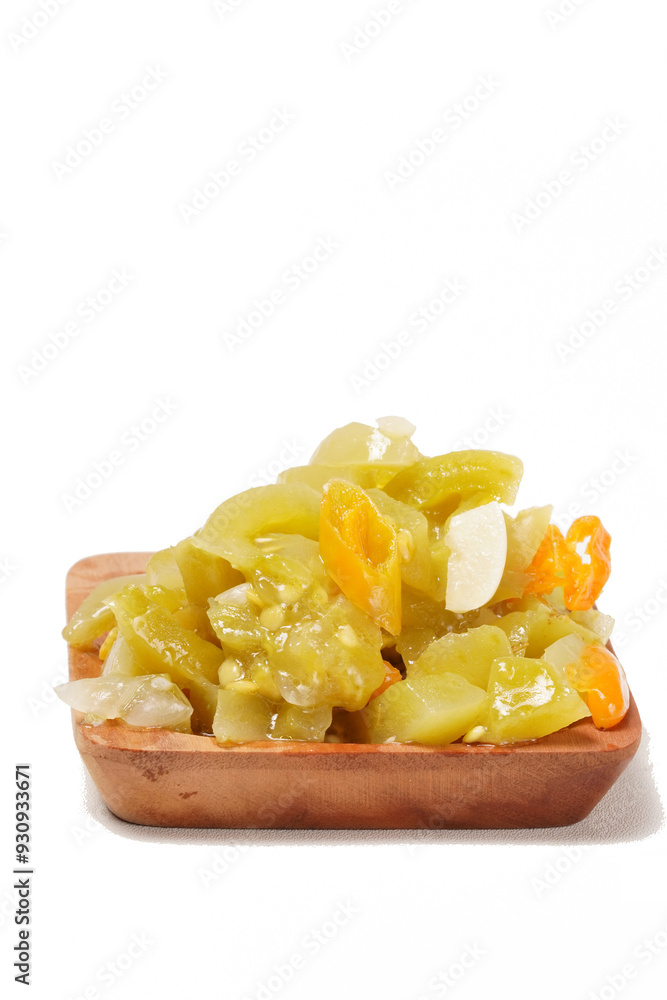 Young tomato sambal with garlic, spices, green tomatoes, and bird's eye chili, served on a wooden plate and photographed against a white background. Young tomato sambal with garlic, spices, green tomatoes, and bird's eye chili, served on a wooden plate and photographed against a white background.