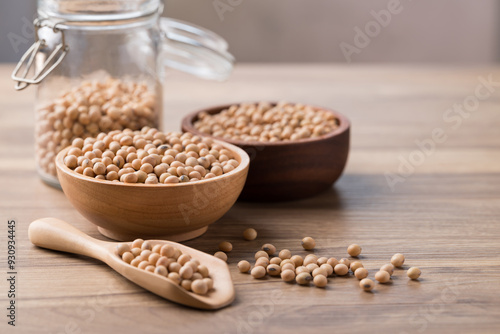 Soy bean seeds in wooden bowl, glass jar and spoon on wooden background photo