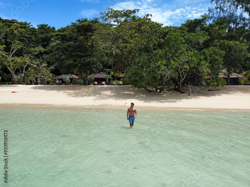 Young man walking on tropical beach of Koh Kradan with transparent water and bungalows in the background, Thailand photo