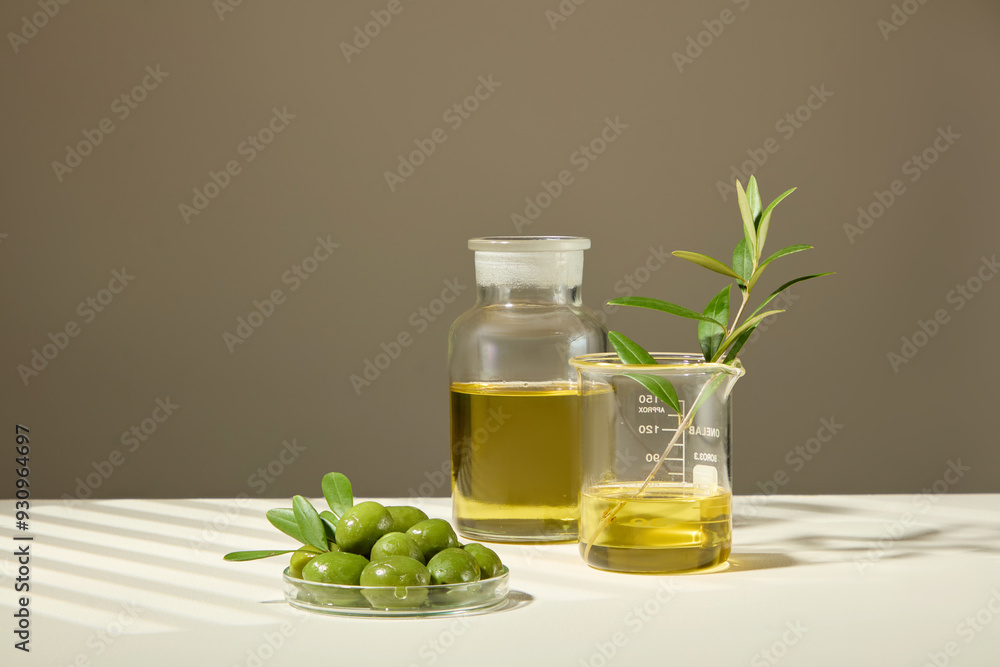 Concept showcases a petri dish filled with olives, olive extract, and branches contained in beaker and large glass jar on a brown background with a white table. The natural concept Concept showcases a petri dish filled with olives, olive extract, and branches contained in beaker and large glass jar on a brown background with a white table. The natural concept