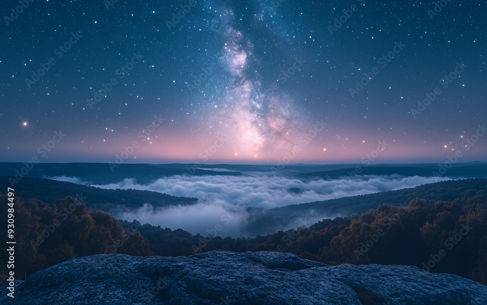 Naklejka premium A breathtaking view of the Milky Way galaxy over a foggy forest landscape, with a starry night sky.