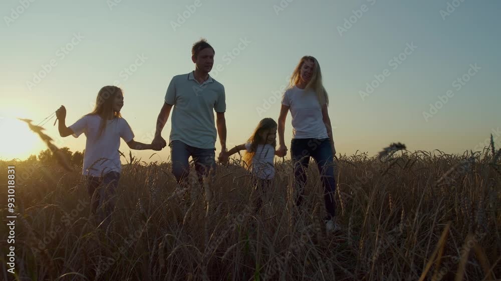 Cheerful family walks through field of wheat. Parents hold children by the hands Cheerful family walks through field of wheat. Parents hold children by the hands