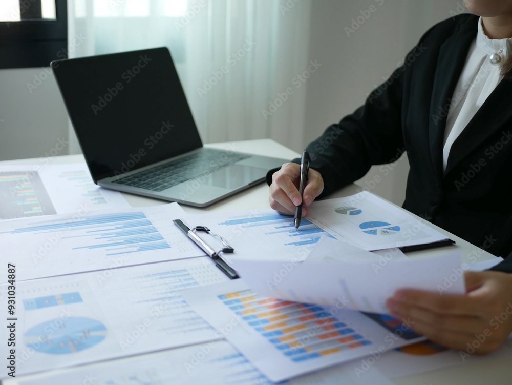 Asian businesswoman holding a pen sits at a table and reads a financial graph showing results about the investment and planning process of successful business growth Asian businesswoman holding a pen sits at a table and reads a financial graph showing results about the investment and planning process of successful business growth