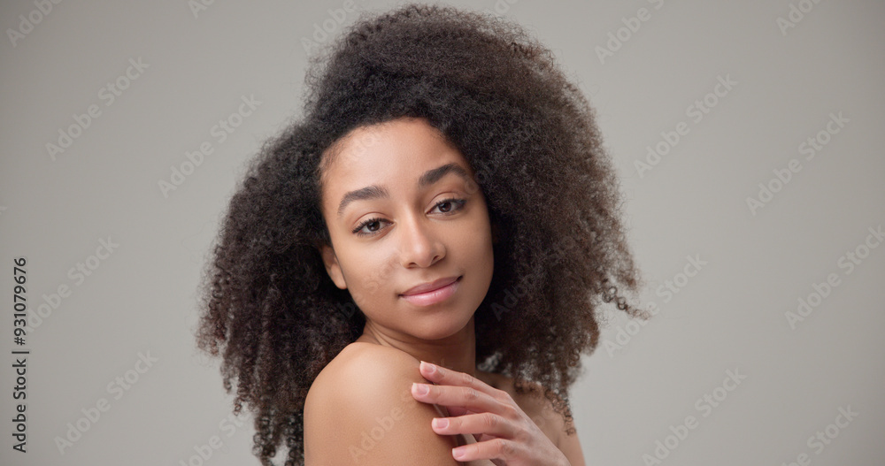 Beauty and healthcare concept - beautiful African American woman with curly afro hairstyle and clean, healthy skin touches her cheek and face with her hand, posing and looking at the camera Beauty and healthcare concept - beautiful African American woman with curly afro hairstyle and clean, healthy skin touches her cheek and face with her hand, posing and looking at the camera