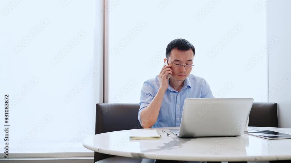 Young asian businessman with digital tablet and laptop talking on mobile phone at desk in office, slow motion video Young asian businessman with digital tablet and laptop talking on mobile phone at desk in office, slow motion video