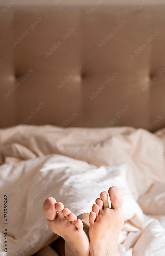 Bare feet peeking out from under blanket on bed. Bare feet peeking out from under blanket on bed.