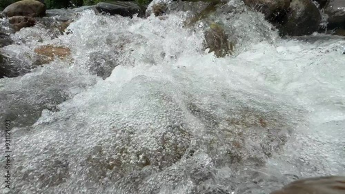 The stream flows over the rocks, creating many small bubbles.