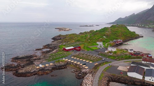 Wide aerial shot of Reine village in Lofoten, northern Norway. Red cottages or houses, cod fish drying racks, waterfront and mountain range in the background. Algae or glacial runoff makes water green photo