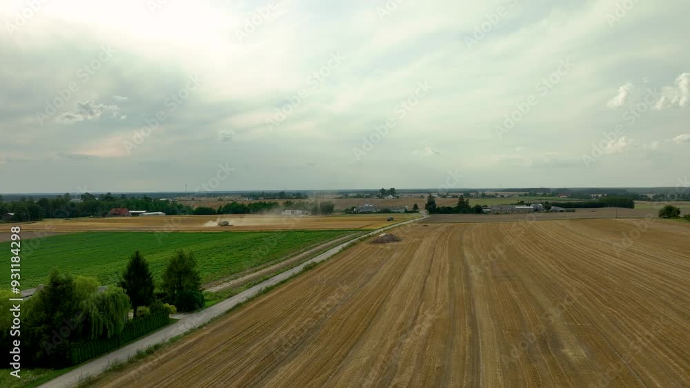 Aerial view of a rural landscape with a distant harvester working in fields under a cloudy sky. Aerial view of a rural landscape with a distant harvester working in fields under a cloudy sky.