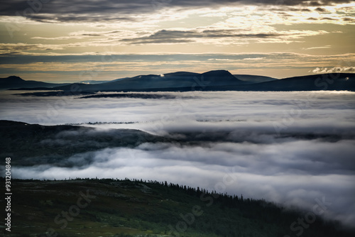 A scenic view of the golden sunlight in the morning fog-filled valley in the Idre, Dalarna Mountains of Sweden, with rolling hills and a cloudy sky