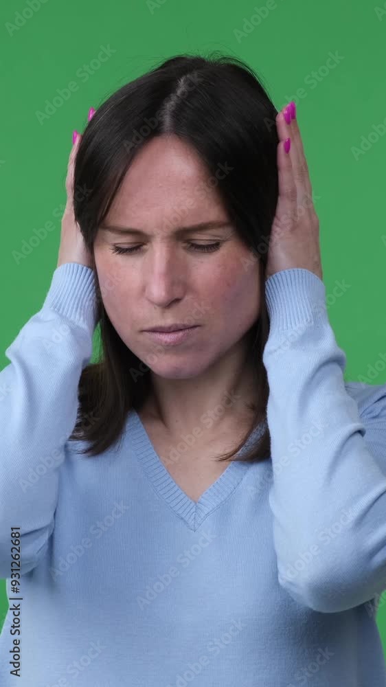 Upset Caucasian middle aged woman covering ears for noise protection standing on green background. Nothing hear concept. Vertical video. Upset Caucasian middle aged woman covering ears for noise protection standing on green background. Nothing hear concept. Vertical video.