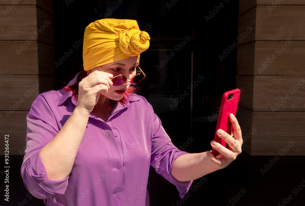 Happy and funny cool lady with fashionable clothes on dark background look to the phone with different emotions - adult asian with extravagant style, concepts about lifestyle, fasion and elderly