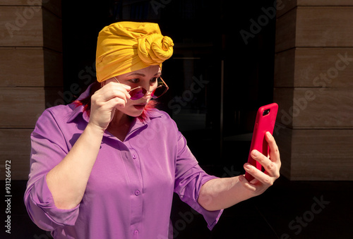 Obraz na płótnie Happy and funny cool lady with fashionable clothes on dark background look to the phone with different emotions - adult asian with extravagant style, concepts about lifestyle, fasion and elderly w salonie