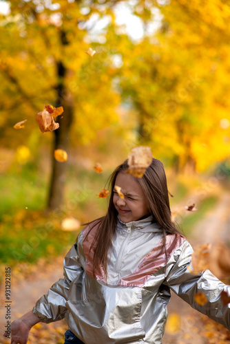 cheerful girl in autumn park throwing yellow leaves in the air