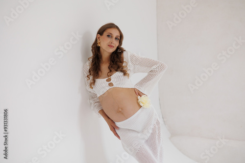 Beautiful pregnant woman in white separate dress with rope in hands. Big pregnant belly. Pretty woman smile, waiting child. Light play on woman's body and face