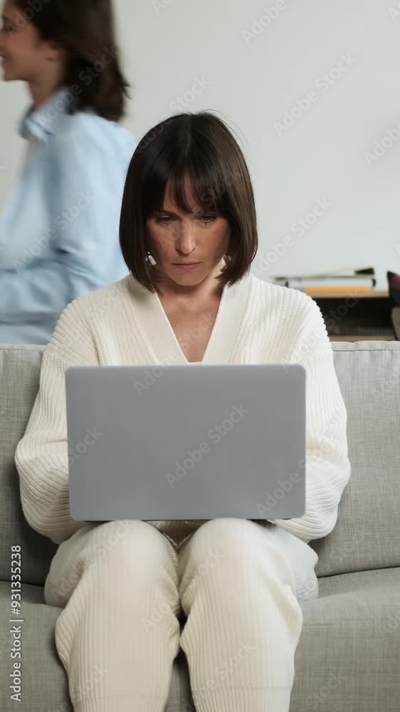 Exhausted and unhappy Caucasian mother working using laptop, suffering from headache while children running around at home living room. Domestic chaos concept. Vertical video. Exhausted and unhappy Caucasian mother working using laptop, suffering from headache while children running around at home living room. Domestic chaos concept. Vertical video.