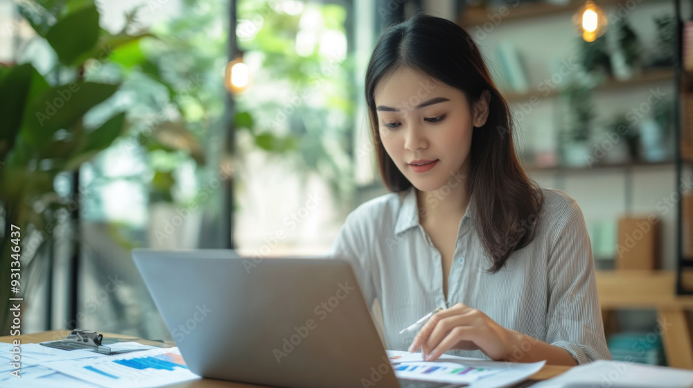 Young Asian woman reviewing her finances on a laptop, planning deductions and expenses Young Asian woman reviewing her finances on a laptop, planning deductions and expenses
