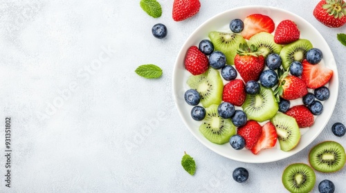 A bowl of fresh fruit salad featuring sliced strawberries, kiwis, and blueberries, garnished with mint leaves, on a light background.