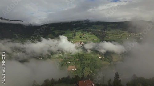 Aerial view of Villanders village enveloped in morning clouds, surrounded by lush green fields and forested hills in a picturesque mountain valley. photo