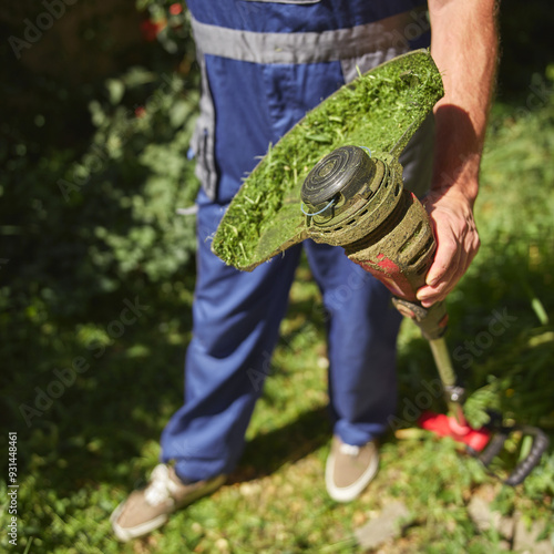 Gardener with a grass trimmer cutting overgrown grass and weeds around the building and changing the worn string. photo