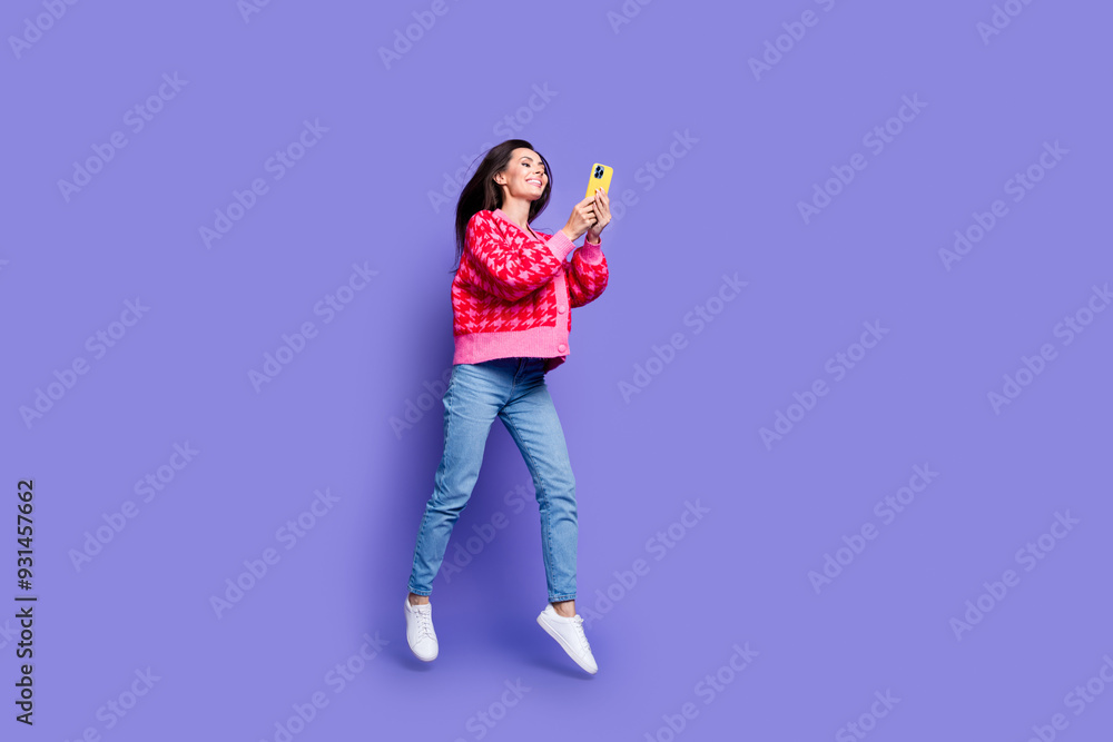 Full length photo of adorable lovely girl wear pink cardigan jumping texting modern device empty space isolated purple color background Full length photo of adorable lovely girl wear pink cardigan jumping texting modern device empty space isolated purple color background