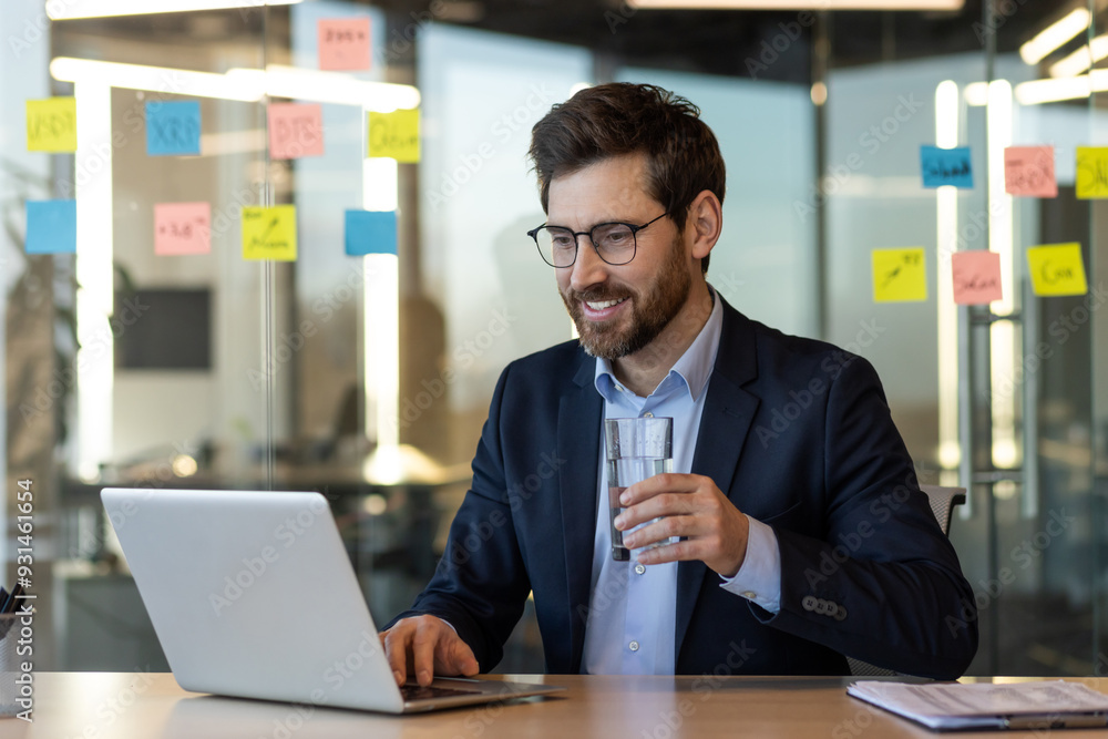 Confident business professional using laptop in modern office setting. Engaged in work while holding drink, conveying focus and relaxation. Confident business professional using laptop in modern office setting. Engaged in work while holding drink, conveying focus and relaxation.
