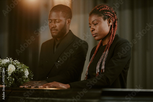 Crying African American woman and doleful man touching coffin