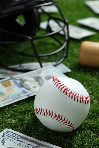 Baseball ball, bat, helmet and dollar banknotes on green grass outdoors photo