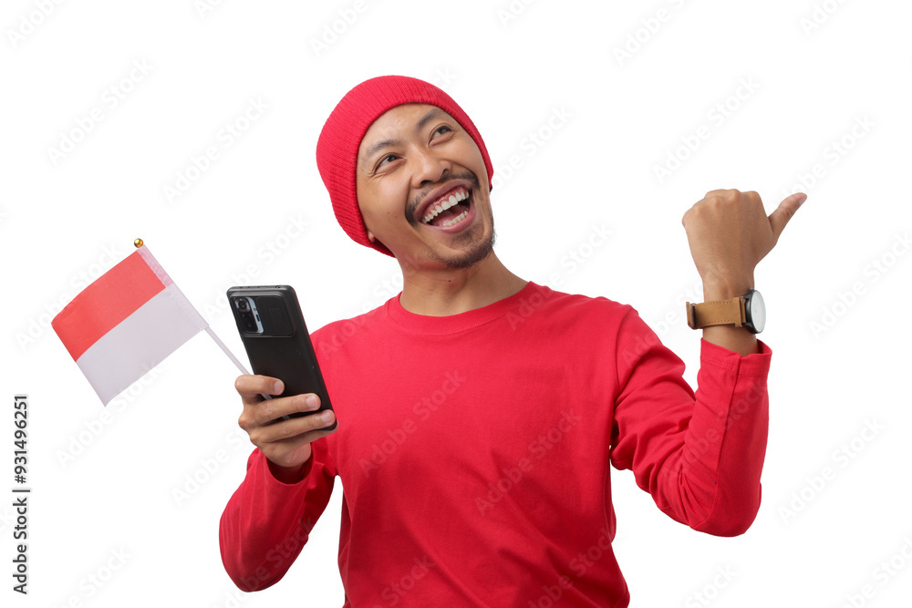 Indonesian man in a red long sleeve shirt points at empty copy space while holding the Indonesian flag and phone during Indonesia Independence Day Celebration on August 17 isolated on white background Indonesian man in a red long sleeve shirt points at empty copy space while holding the Indonesian flag and phone during Indonesia Independence Day Celebration on August 17 isolated on white background