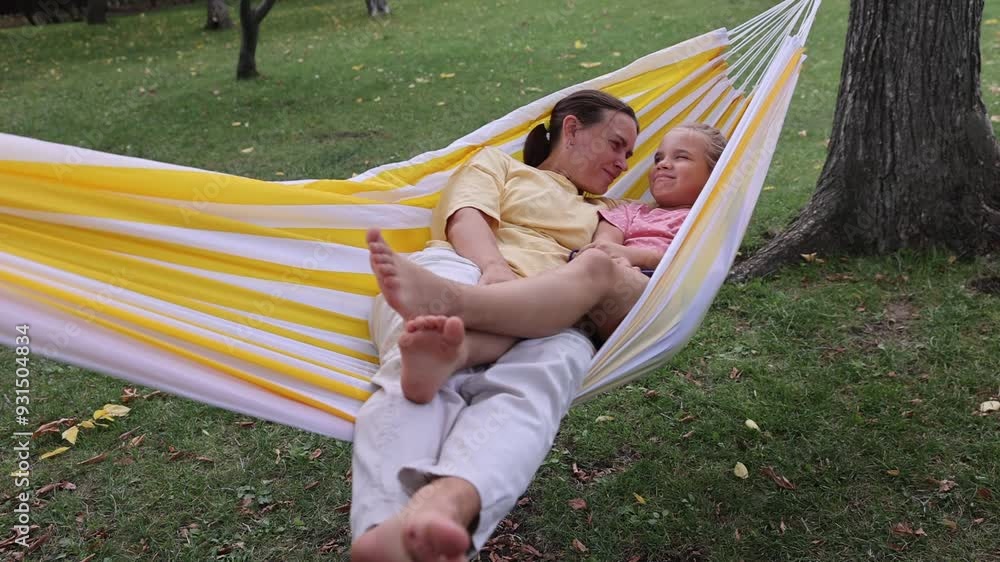 mom and child daughter swing in a hammock in a summer park or garden. Concept of friendly family.