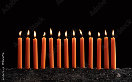 Row of orange candles with flames in the dirt ground and black background.