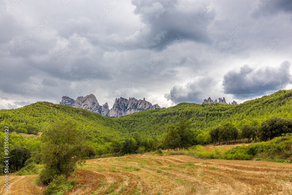 Obraz premium Campos de cultivo junto a bosques y montaña de Montserrat un día nublado y tormentoso