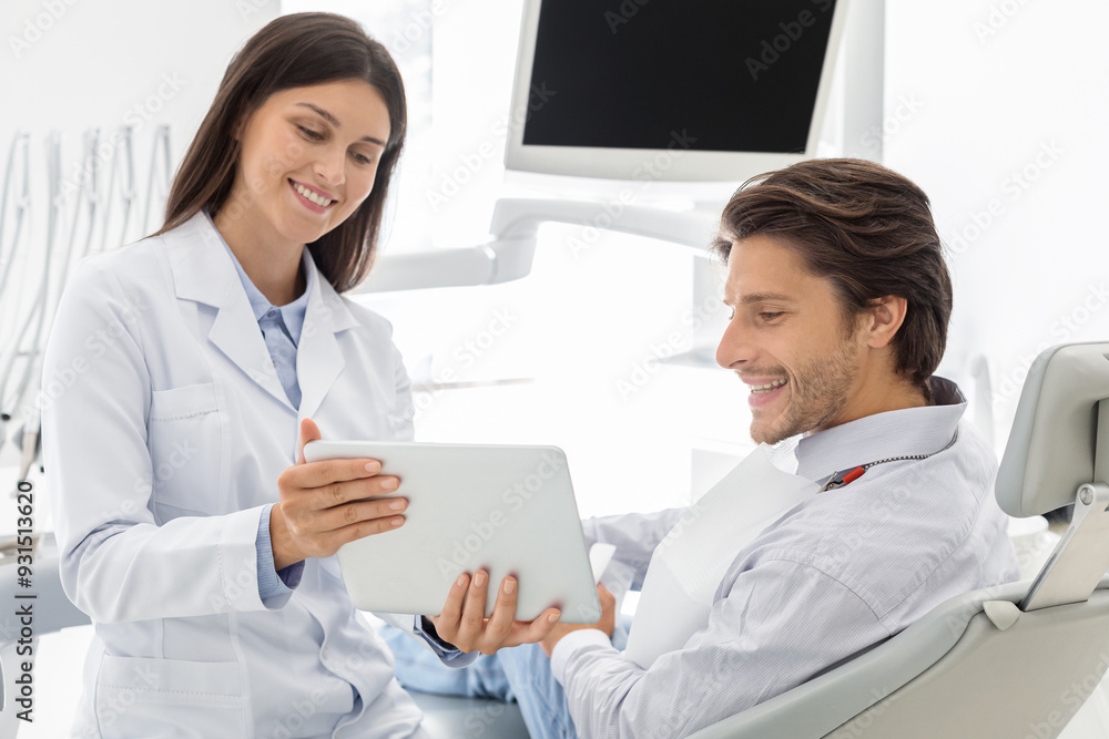 Cheerful female dentist showing patient results of treatment on digital tablet, dental cabinet