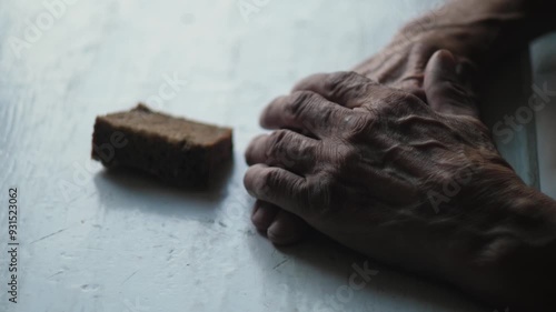 old man's hands and piece of rye bread on empty table, need loneliness and hunger in old age concept, pensioner looks at last piece of food or bread photo