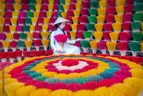 A young Vietnamese woman in a white national costume arranges colorful incense sticks in Hue, Vietnam.