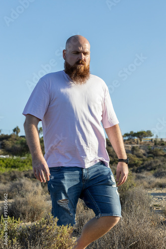 Bald man with beard and pink t-shirt walking through the countryside.