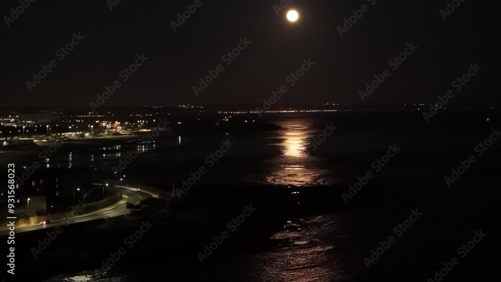 Bright moonlight casts shimmering reflections on the water, illuminating the coastline and city lights in the evening. Captured in Lisbon, Portugal Bright moonlight casts shimmering reflections on the water, illuminating the coastline and city lights in the evening. Captured in Lisbon, Portugal