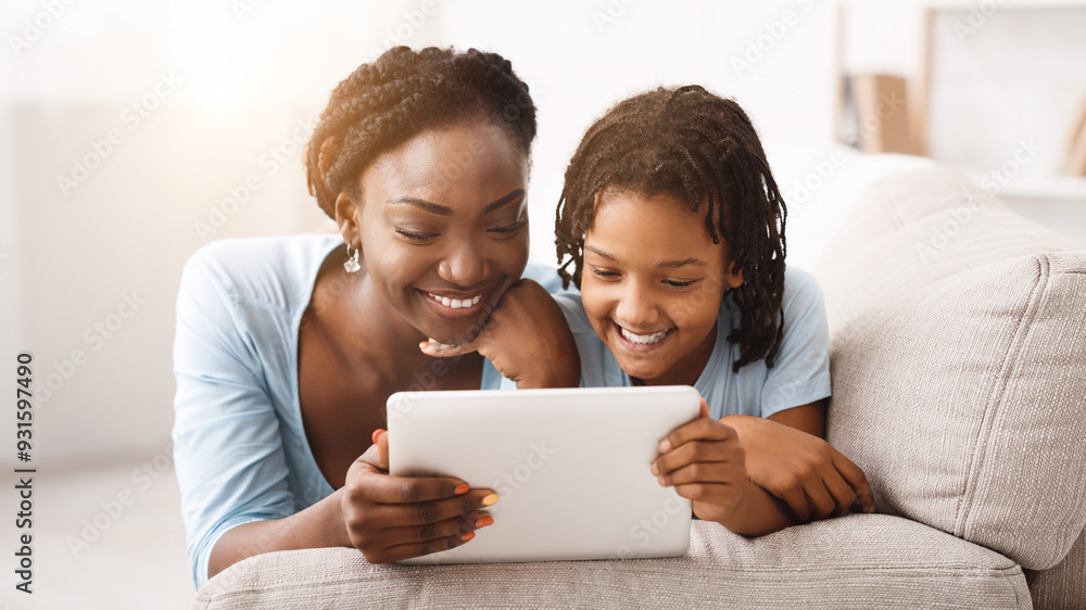 African Mom And Daughter Watching Cartoons Together On Digital Tablet, Lying On Couch. Free space African Mom And Daughter Watching Cartoons Together On Digital Tablet, Lying On Couch. Free space